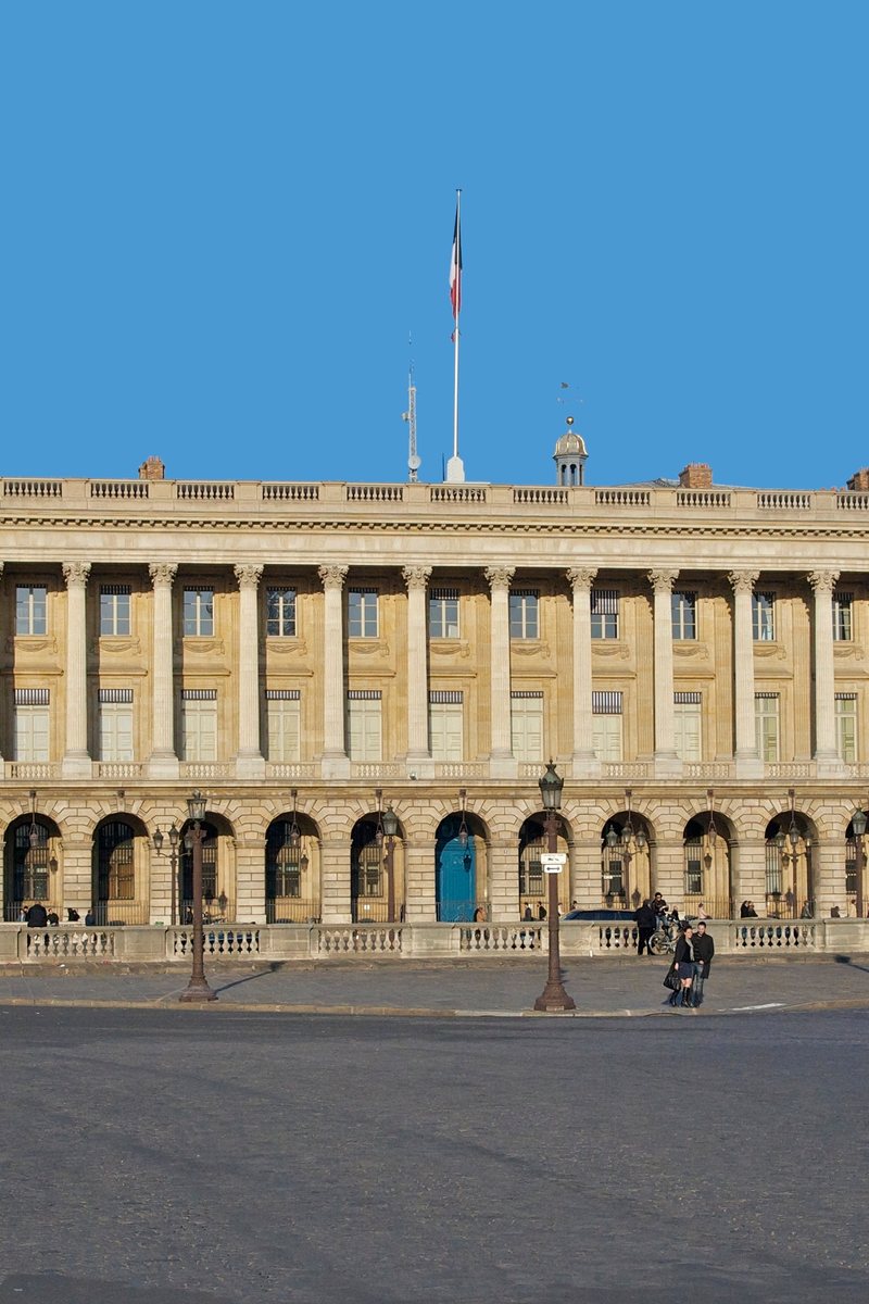 The colonnaded façade of the Hôtel de la Marine on the Place de la Concorde in Paris — a long neoclassical peristyle of paired Corinthian columns above a stone arcade, glowing in late-afternoon light. Paris, France.